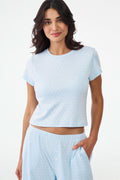 A woman with wavy dark hair gives a slight smile while wearing the Roller Rabbit Hearts Tonal Classic Baby Tee, standing against a plain white background.