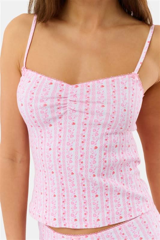 A woman wears the Hearts Vine Greene Cami pajama set by Roller Rabbit in pink and white with a small floral pattern, standing against a plain light background.
