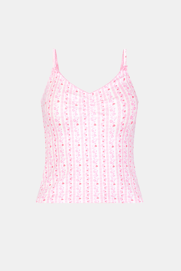 A woman wears the Hearts Vine Greene Cami pajama set by Roller Rabbit in pink and white with a small floral pattern, standing against a plain light background.