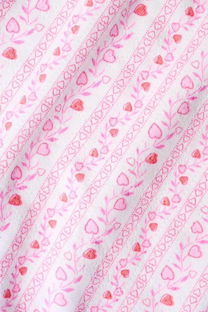 A woman stands facing forward with her hands behind her back, wearing the Roller Rabbit Hearts Vine Orchard Slip Dress, which features a pink and white floral pattern and a lace-trimmed V-neckline.