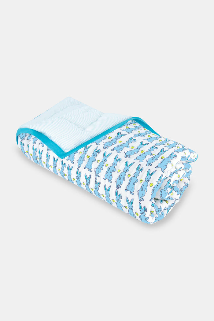 The Roller Rabbit Hoppy Baby Quilt features a playful blue and yellow Hoppy the Bunny pattern on white cotton, accented with a blue border and shown rolled up on a light surface.