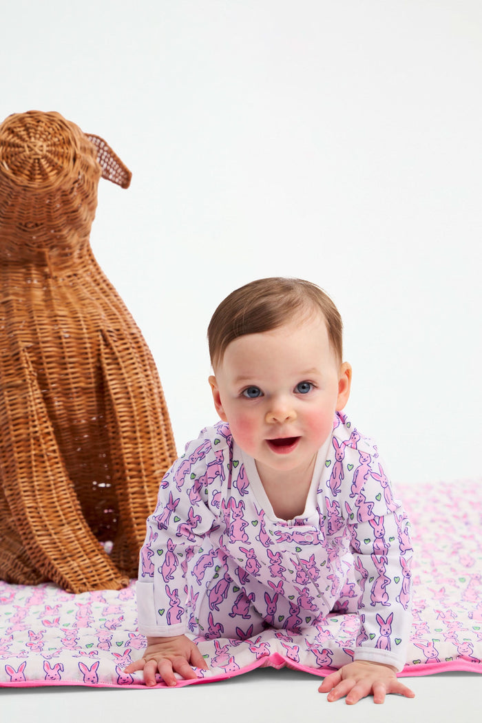 The Hoppy Baby Quilt by Roller Rabbit is a folded cotton quilt with a pink border and a hand-block print of pink and purple rabbits, shown on a plain white background.