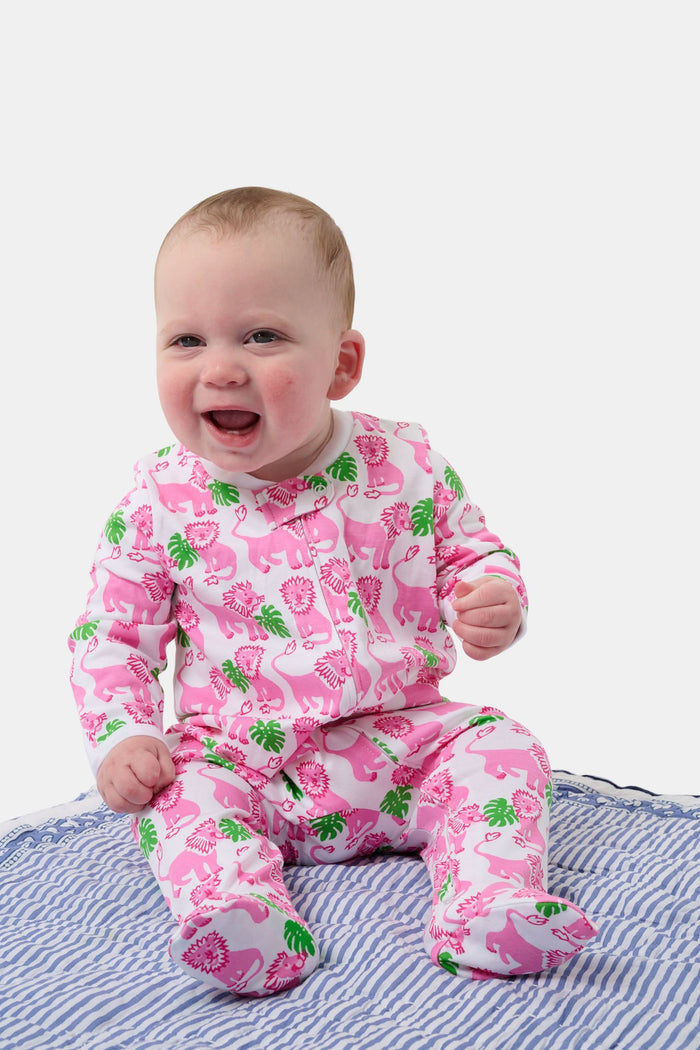 A smiling baby with light skin and short hair sits on a blue and white striped blanket wearing the Roller Rabbit Infant Leo The Lion Zipper Footie, made from soft Pima cotton with a convenient two-way zipper for easy dressing.