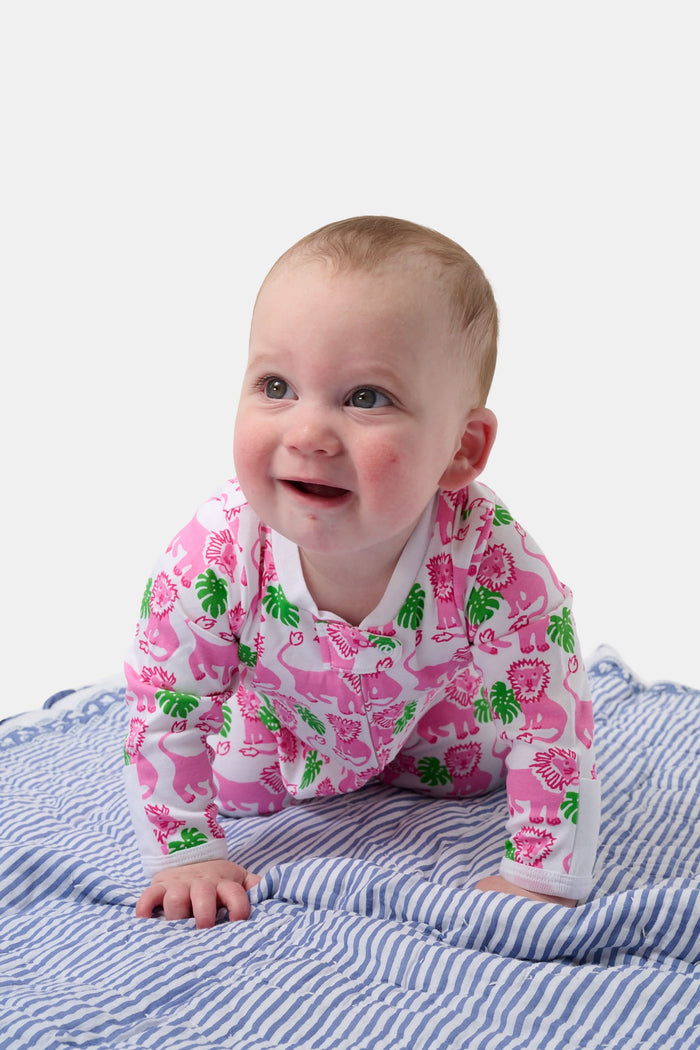 A smiling baby with light skin and short hair sits on a blue and white striped blanket wearing the Roller Rabbit Infant Leo The Lion Zipper Footie, made from soft Pima cotton with a convenient two-way zipper for easy dressing.