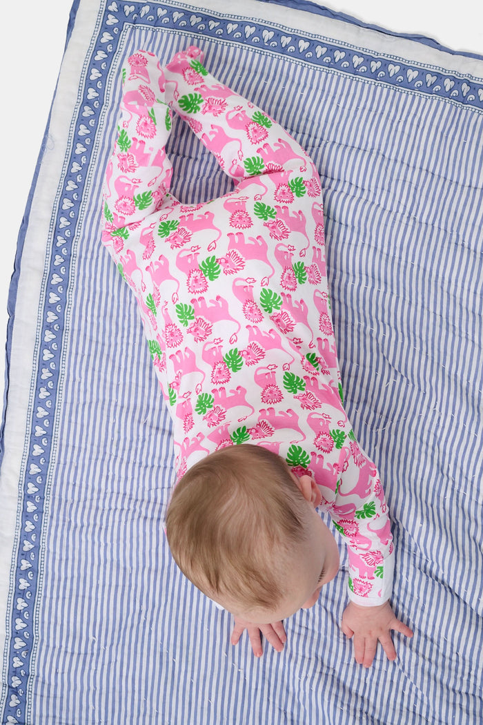 A smiling baby with light skin and short hair sits on a blue and white striped blanket wearing the Roller Rabbit Infant Leo The Lion Zipper Footie, made from soft Pima cotton with a convenient two-way zipper for easy dressing.