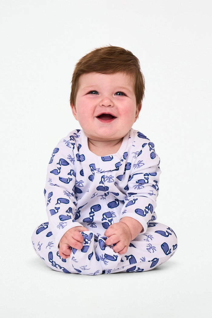 The Roller Rabbit Infant Moby Zipper Footie is a white, long-sleeve, footed pajama with blue sunglasses and palm trees, crafted from 100 Pima Cotton and features a front zipper from neck to leg.