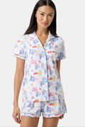 A woman with long dark hair wears Roller Rabbit’s Italy Monkey Polo Pajamas, a playful Pima Cotton set featuring cartoon animals and Italian motifs. The short-sleeved, button-up top pairs perfectly with the matching shorts.