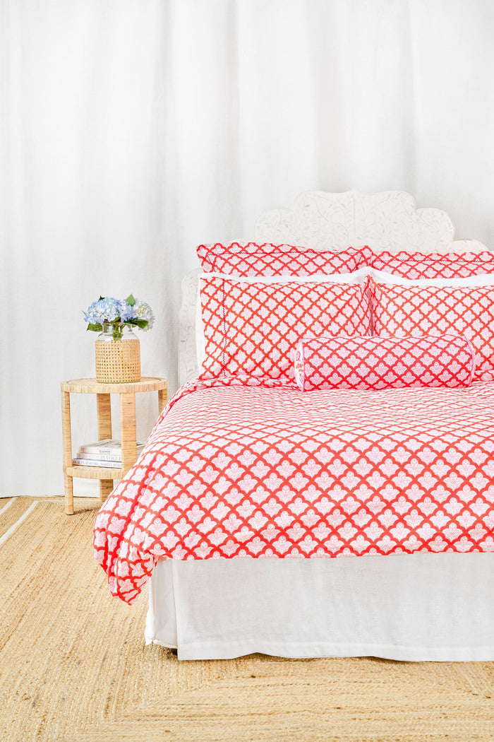 The Jemina Duvet Cover by Roller Rabbit features a red and white heart-patterned print, paired with matching pillow shams and crisp white sheets. Neatly arranged pillows and an ornate white headboard complete the airy, inviting bedding look.
