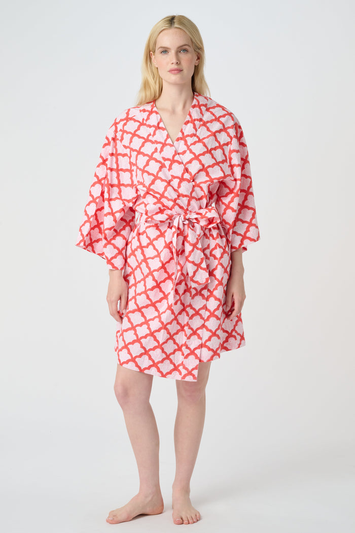 A woman stands barefoot in the Roller Rabbit Jemina Kimono, a knee-length cotton design with wide sleeves, a belt, and a red and white Jemina print. She faces forward against a plain light background.