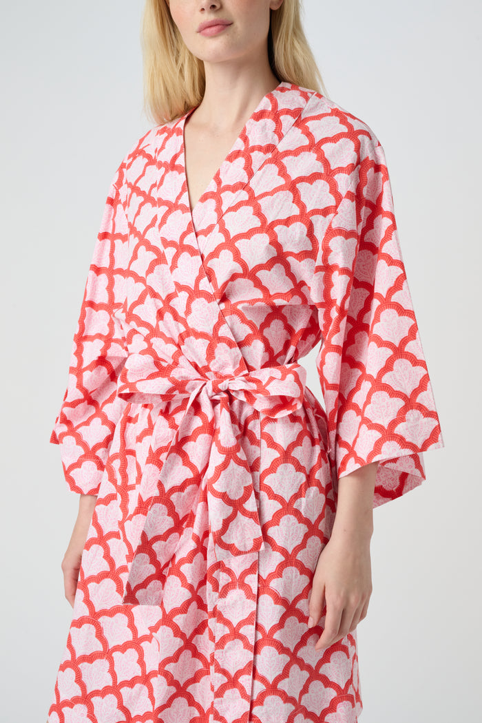 A woman stands barefoot in the Roller Rabbit Jemina Kimono, a knee-length cotton design with wide sleeves, a belt, and a red and white Jemina print. She faces forward against a plain light background.