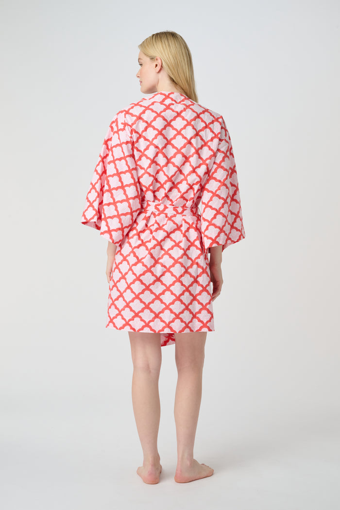 A woman stands barefoot in the Roller Rabbit Jemina Kimono, a knee-length cotton design with wide sleeves, a belt, and a red and white Jemina print. She faces forward against a plain light background.