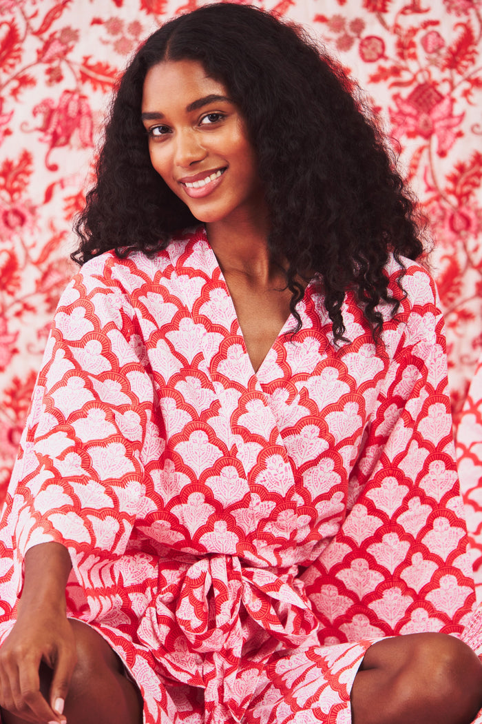 A woman stands barefoot in the Roller Rabbit Jemina Kimono, a knee-length cotton design with wide sleeves, a belt, and a red and white Jemina print. She faces forward against a plain light background.
