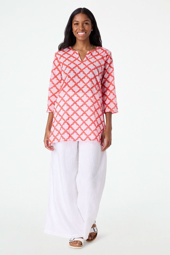 A woman with long dark hair smiles in a relaxed fit, pink and red Jemina Kurta by Roller Rabbit, holding a matching white and pink patterned tote bag against a plain light background.