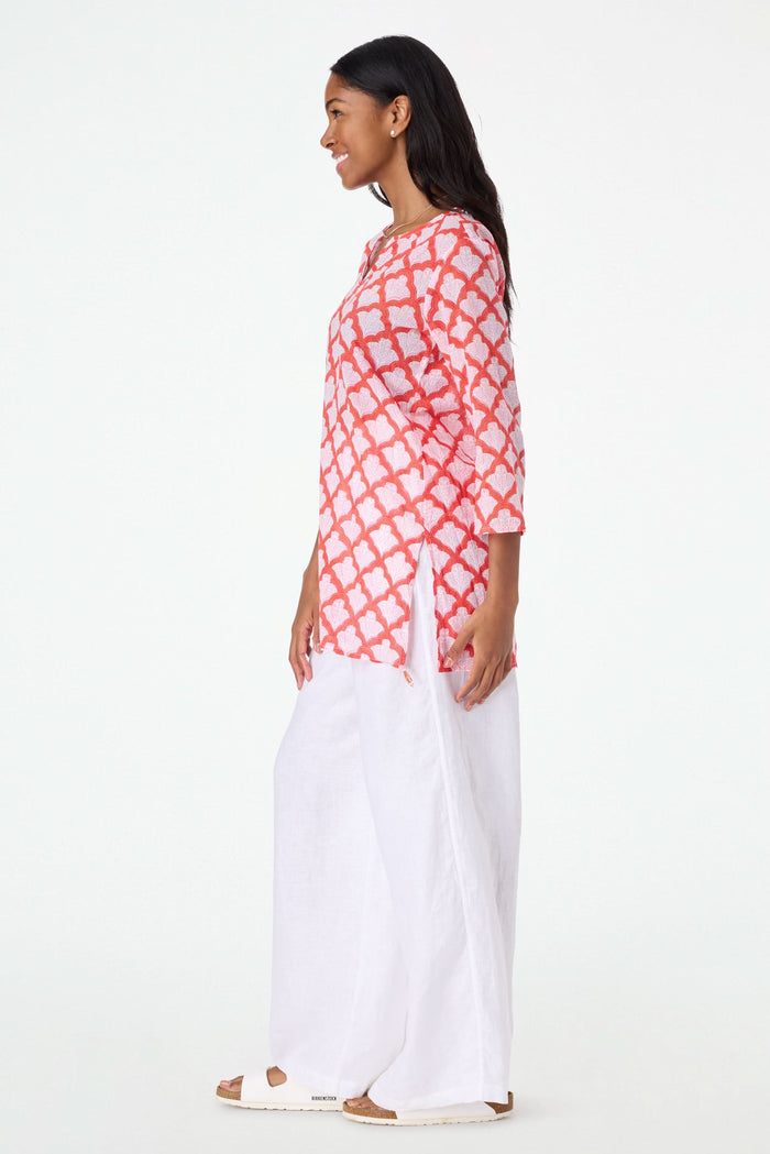 A woman with long dark hair smiles in a relaxed fit, pink and red Jemina Kurta by Roller Rabbit, holding a matching white and pink patterned tote bag against a plain light background.