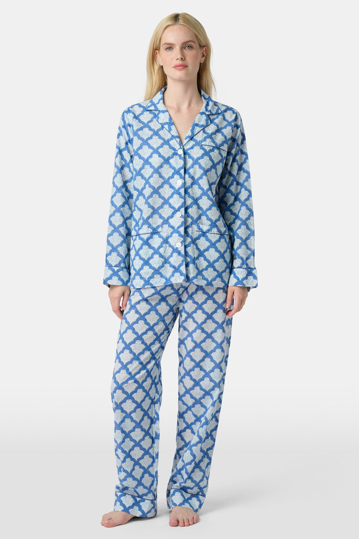 A woman stands barefoot against a plain white background wearing the Roller Rabbit Jemina Loungewear set, featuring a blue and white medallion print button-up long-sleeve top with matching pants.