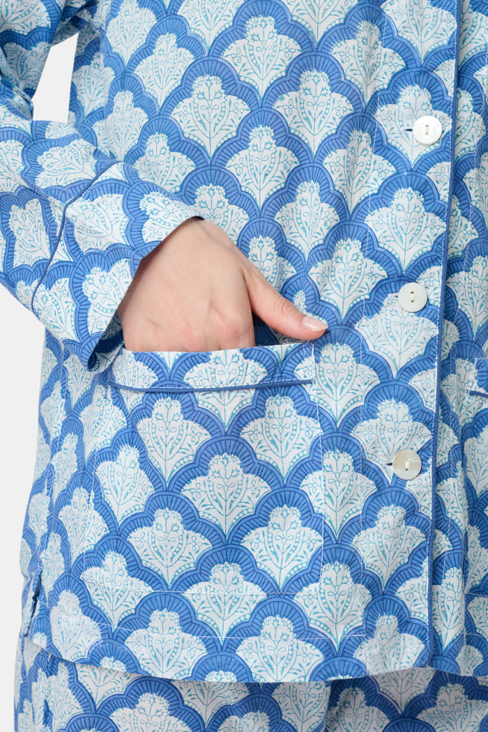 A woman stands barefoot against a plain white background wearing the Roller Rabbit Jemina Loungewear set, featuring a blue and white medallion print button-up long-sleeve top with matching pants.