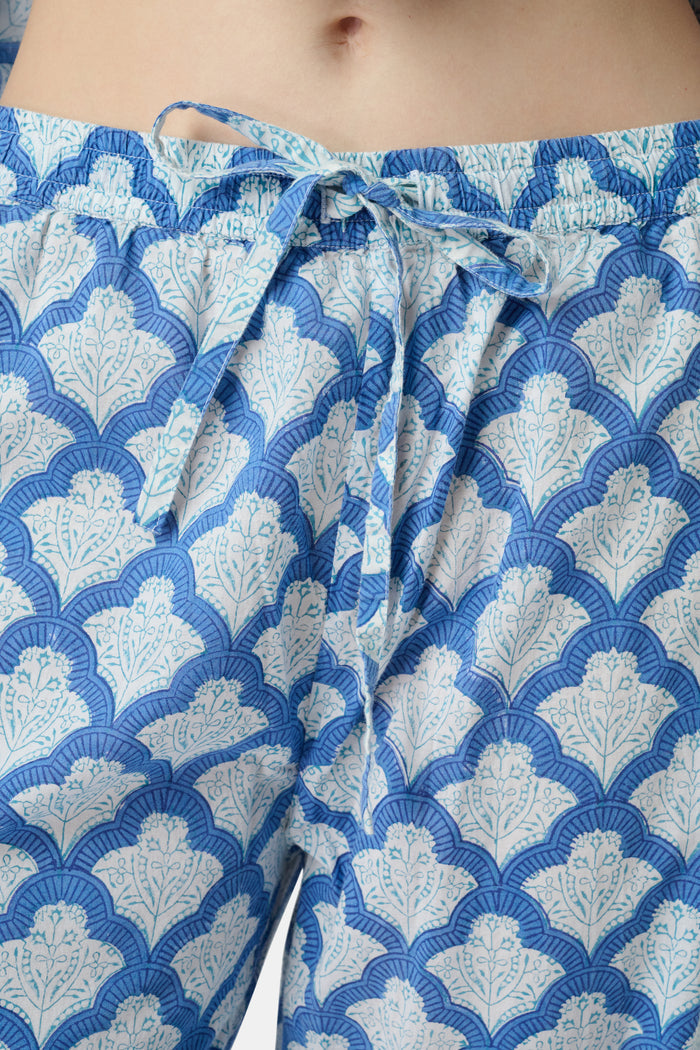 A woman stands barefoot against a plain white background wearing the Roller Rabbit Jemina Loungewear set, featuring a blue and white medallion print button-up long-sleeve top with matching pants.