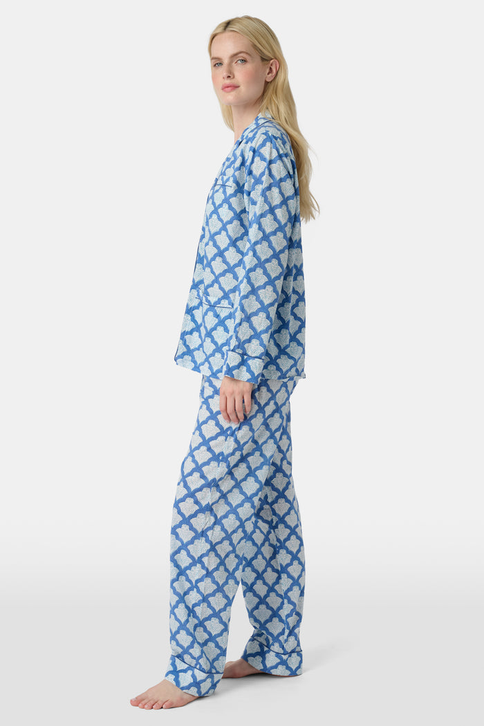 A woman stands barefoot against a plain white background wearing the Roller Rabbit Jemina Loungewear set, featuring a blue and white medallion print button-up long-sleeve top with matching pants.