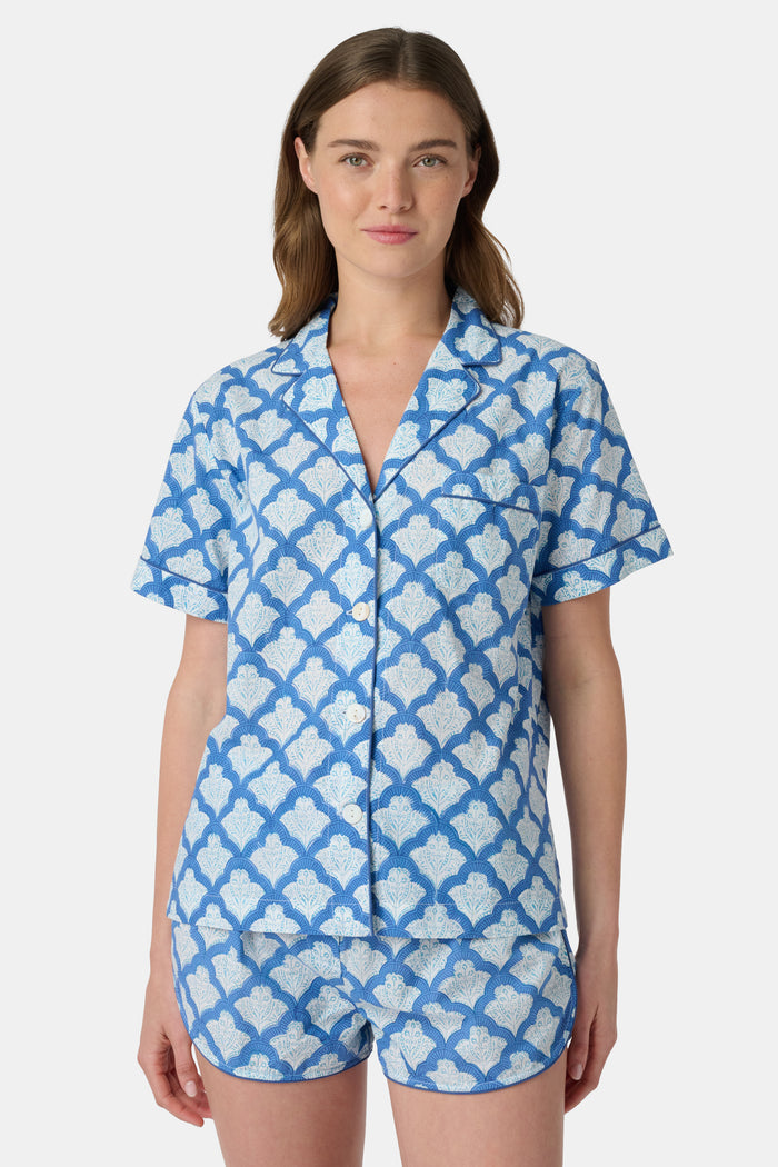 A woman wears the Roller Rabbit Jemina Lulu Set, a cotton pajama set with a matching short-sleeve button-up top and shorts, featuring a blue and white geometric leaf print, standing against a plain light background.