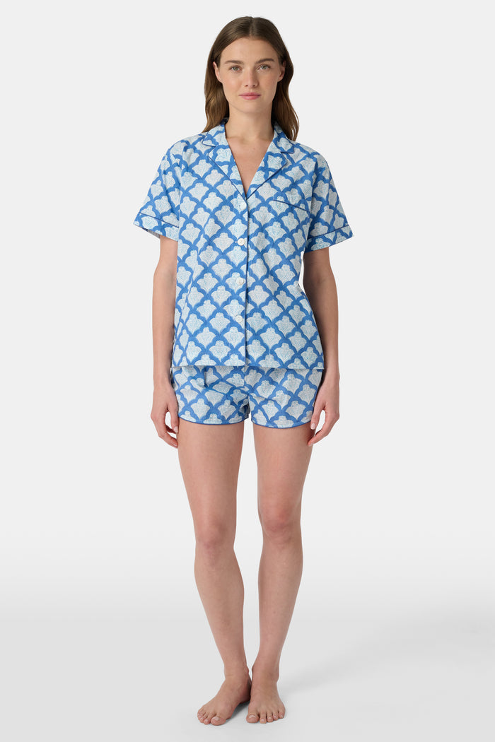 A woman wears the Roller Rabbit Jemina Lulu Set, a cotton pajama set with a matching short-sleeve button-up top and shorts, featuring a blue and white geometric leaf print, standing against a plain light background.