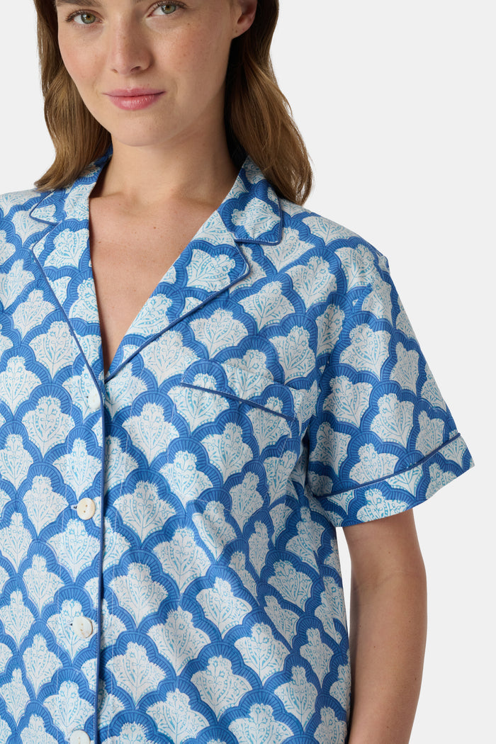 A woman wears the Roller Rabbit Jemina Lulu Set, a cotton pajama set with a matching short-sleeve button-up top and shorts, featuring a blue and white geometric leaf print, standing against a plain light background.