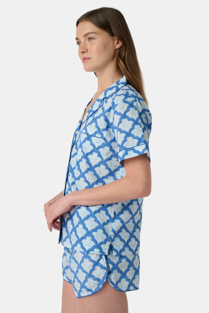 A woman wears the Roller Rabbit Jemina Lulu Set, a cotton pajama set with a matching short-sleeve button-up top and shorts, featuring a blue and white geometric leaf print, standing against a plain light background.