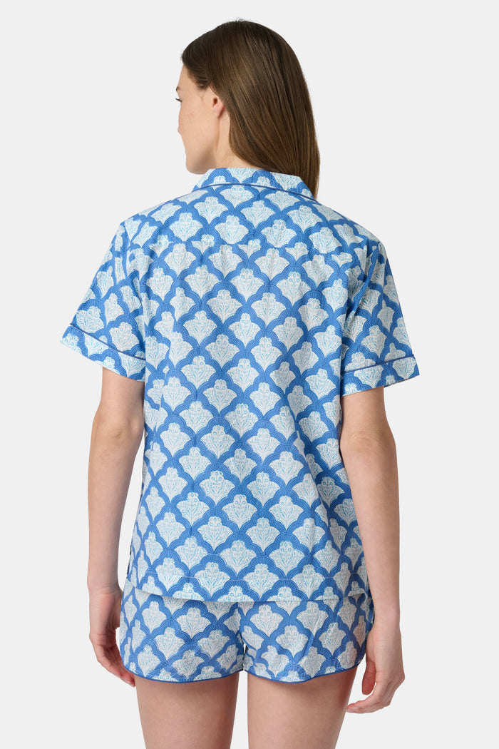 A woman wears the Roller Rabbit Jemina Lulu Set, a cotton pajama set with a matching short-sleeve button-up top and shorts, featuring a blue and white geometric leaf print, standing against a plain light background.