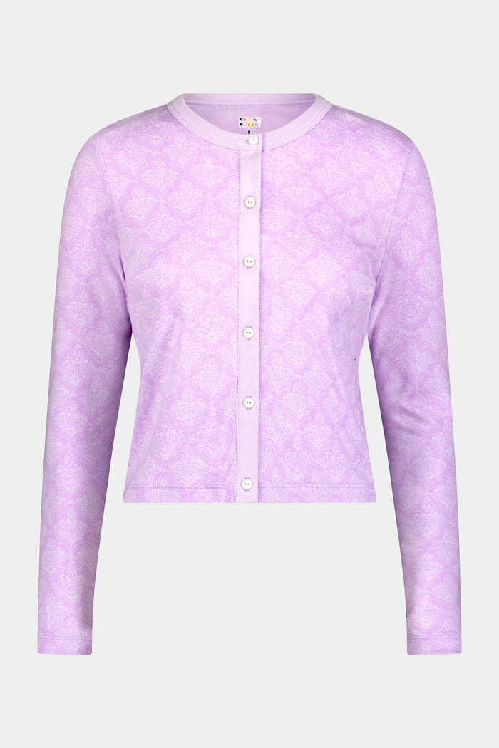 A smiling woman with curly hair wears the Roller Rabbit Jemina Nessa Cardigan pajama set in light purple, standing against a plain white background.