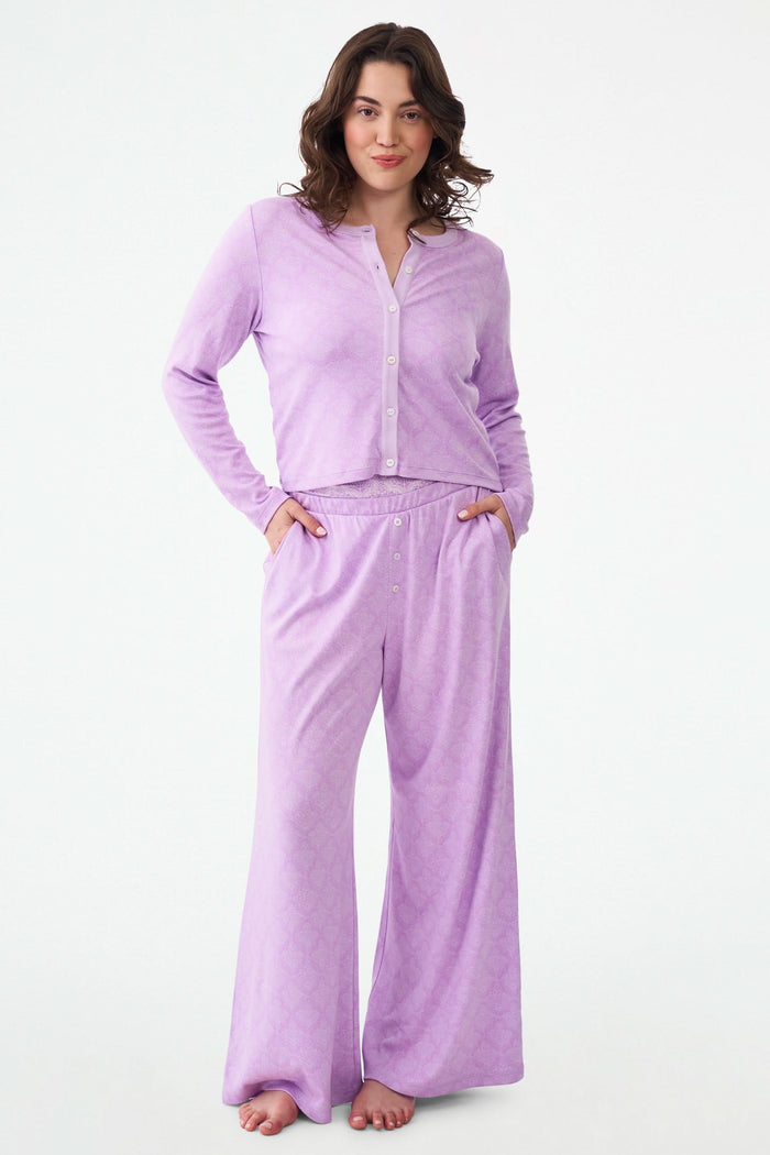 A smiling woman with curly hair wears the Roller Rabbit Jemina Nessa Cardigan pajama set in light purple, standing against a plain white background.