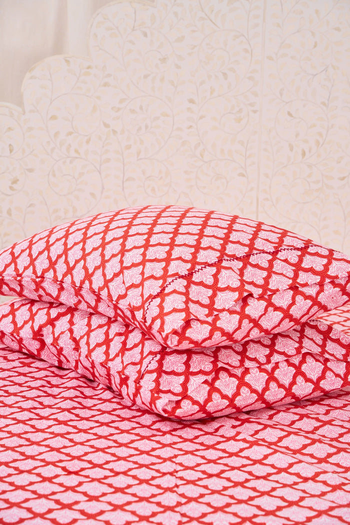 Two stacked Roller Rabbit Jemina Pillowcase Set pillowcases in a red and white print rest on a matching 100 cotton bedsheet, set against a white decorative background.