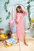 A smiling woman wears the Jemina Punta Long Kurta by Roller Rabbit, standing indoors with colorful bags. She is surrounded by lemons, baskets, greenery, and a light blue wall with a decorative arch in the background.