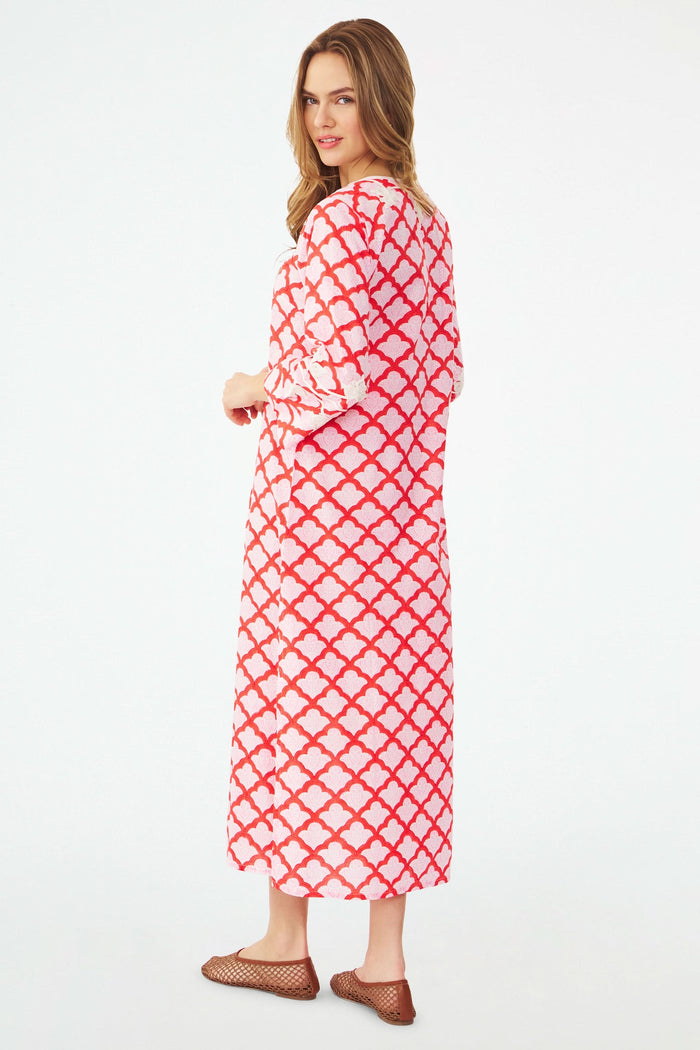 A smiling woman wears the Jemina Punta Long Kurta by Roller Rabbit, standing indoors with colorful bags. She is surrounded by lemons, baskets, greenery, and a light blue wall with a decorative arch in the background.