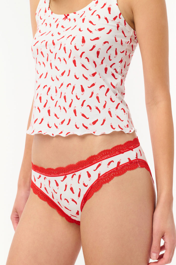 The Jet Set Bikini 4 Pack by Roller Rabbit includes four cotton-modal pairs with lace trim: blue with cherries, light pink with hearts, white with red chili peppers, and red with a geometric design.