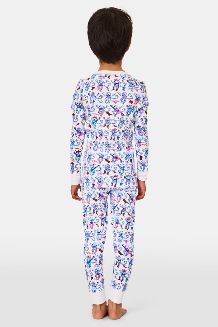 A young child stands smiling, wearing the Roller Rabbit Kids Austin Monkey Pajamas—a super soft pajama set with colorful, long sleeves and a playful cartoon monkey pattern on a white background.