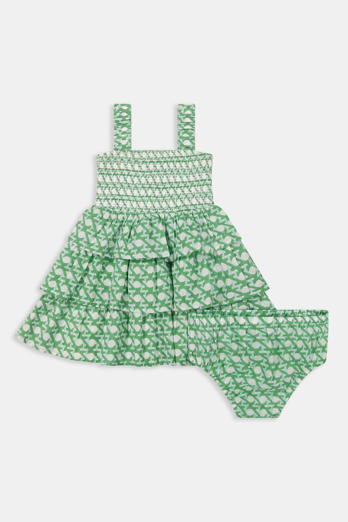 A young girl with curly hair wears the Roller Rabbit Kids Cane Kenia Dress, a green and white patterned cotton tiered dress with wide straps, standing against a plain light background.