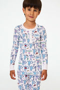 A young child with short dark hair smiles while wearing Roller Rabbit Kids Chicago Monkey Pajamas, featuring colorful cartoon monkeys, hearts, and books on a white background.