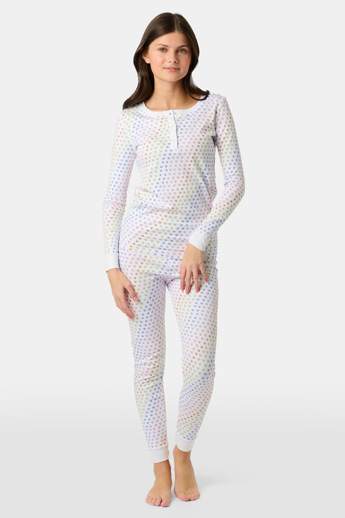 A girl wears Roller Rabbit's Kids Disco Hearts Pajamas, featuring a long-sleeve, buttoned top and matching pants with a colorful rainbow heart print on a light background.