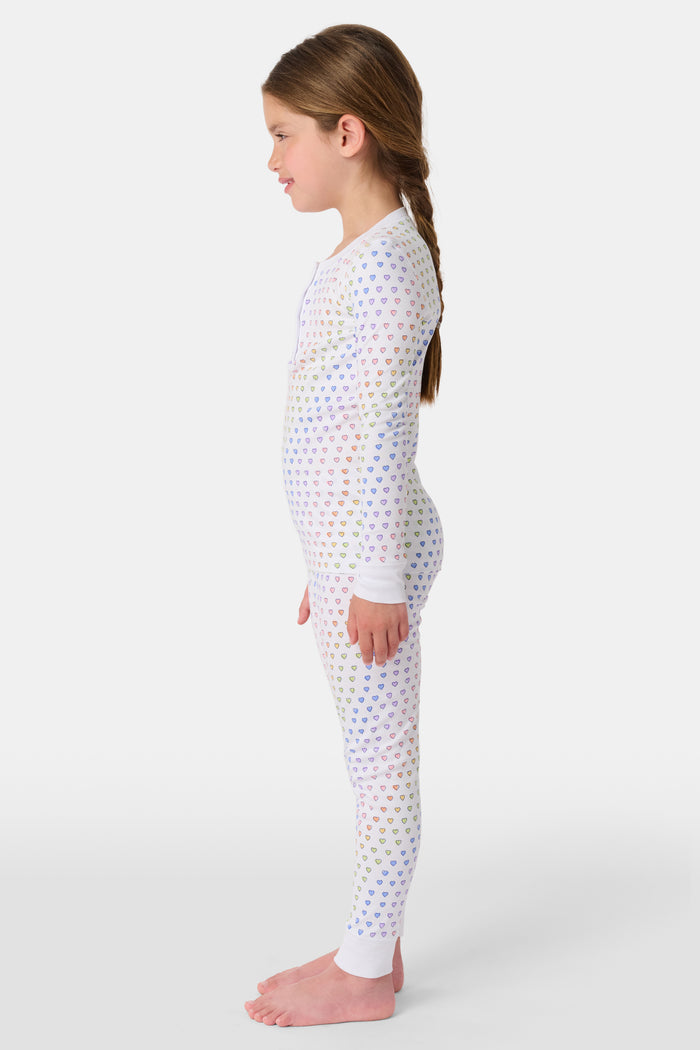 A girl wears Roller Rabbit's Kids Disco Hearts Pajamas, featuring a long-sleeve, buttoned top and matching pants with a colorful rainbow heart print on a light background.