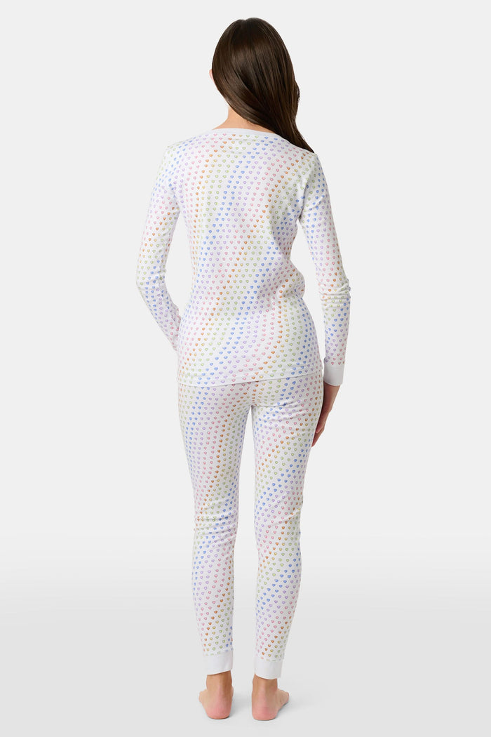A girl wears Roller Rabbit's Kids Disco Hearts Pajamas, featuring a long-sleeve, buttoned top and matching pants with a colorful rainbow heart print on a light background.