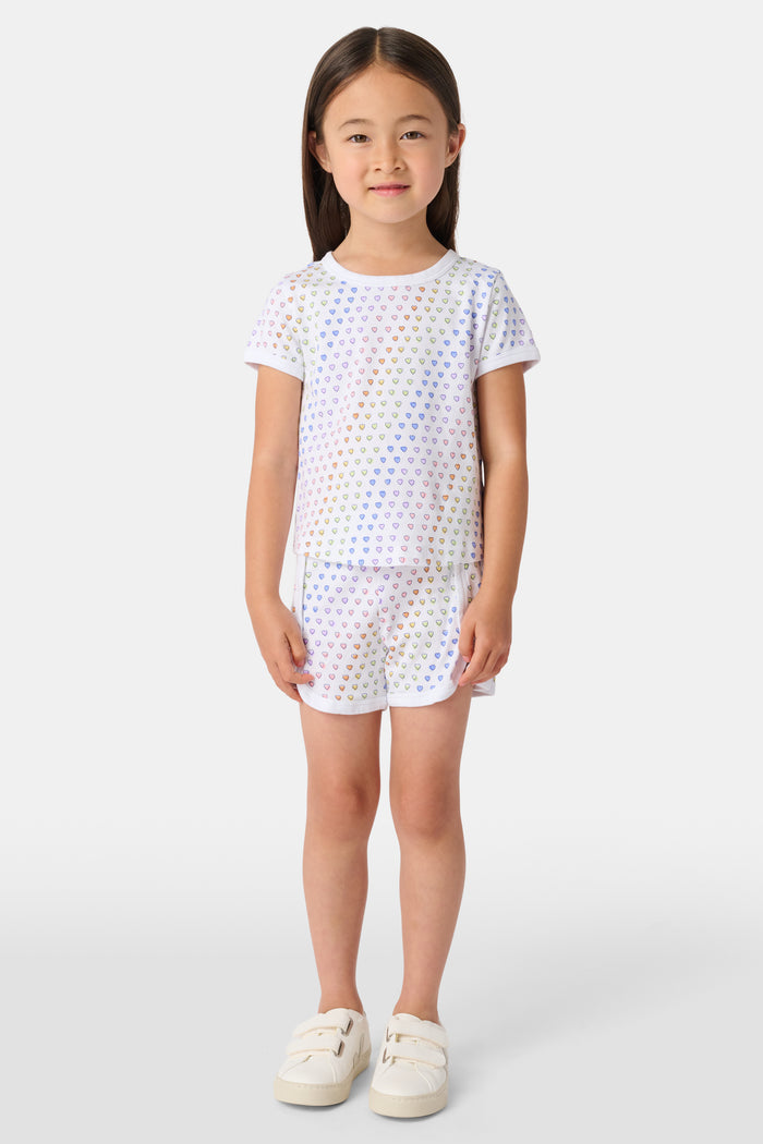 A young child with long brown hair wears the Roller Rabbit Kids Disco Hearts Playa Play Set, smiling while standing against a plain white background.