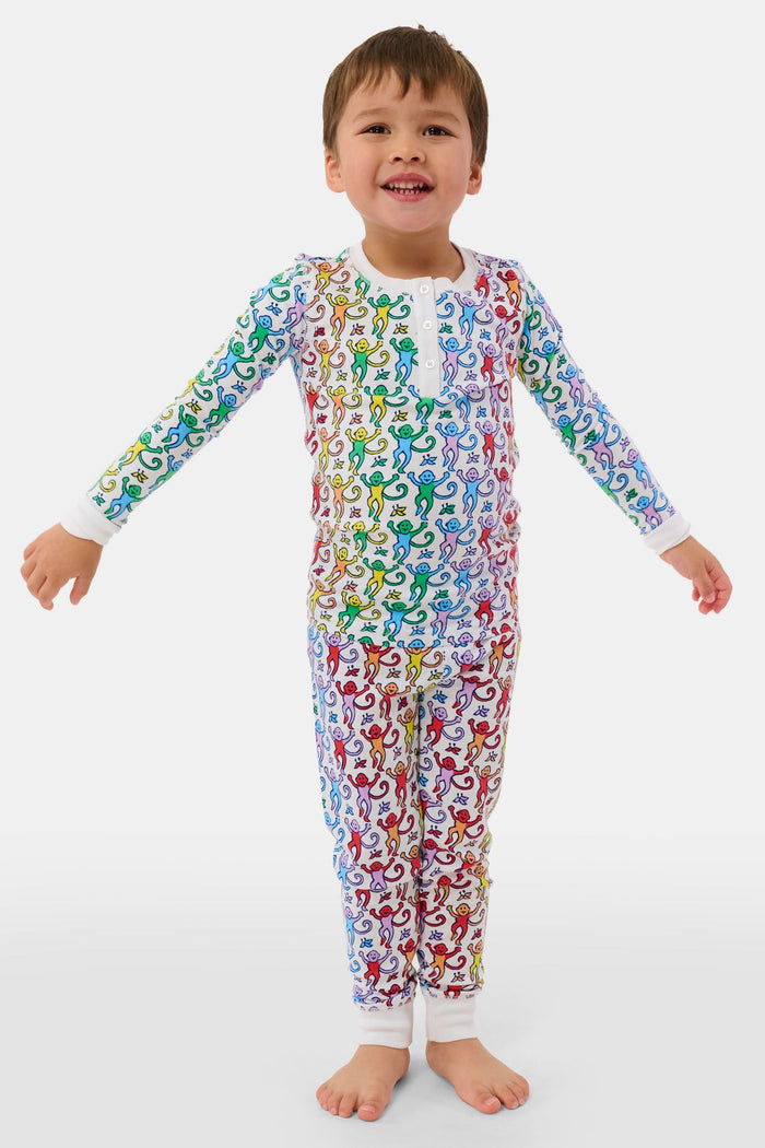 A young child stands barefoot and smiling, wearing Roller Rabbit Kids Disco Monkey Pajamas—crafted from soft 100 pima cotton with a playful monkey print on white—perfect for cozy kids sleepwear.