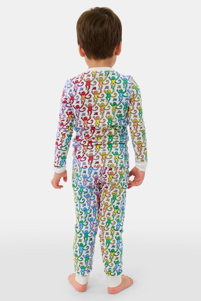 A young child stands barefoot and smiling, wearing Roller Rabbit Kids Disco Monkey Pajamas—crafted from soft 100 pima cotton with a playful monkey print on white—perfect for cozy kids sleepwear.