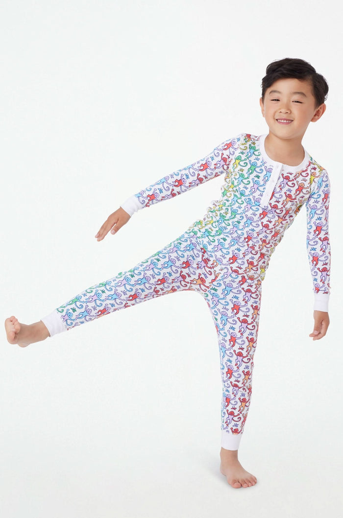 A young child stands barefoot and smiling, wearing Roller Rabbit Kids Disco Monkey Pajamas—crafted from soft 100 pima cotton with a playful monkey print on white—perfect for cozy kids sleepwear.