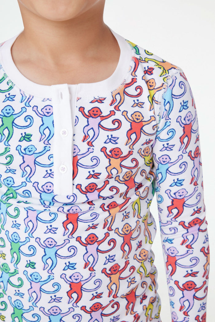 A young child stands barefoot and smiling, wearing Roller Rabbit Kids Disco Monkey Pajamas—crafted from soft 100 pima cotton with a playful monkey print on white—perfect for cozy kids sleepwear.