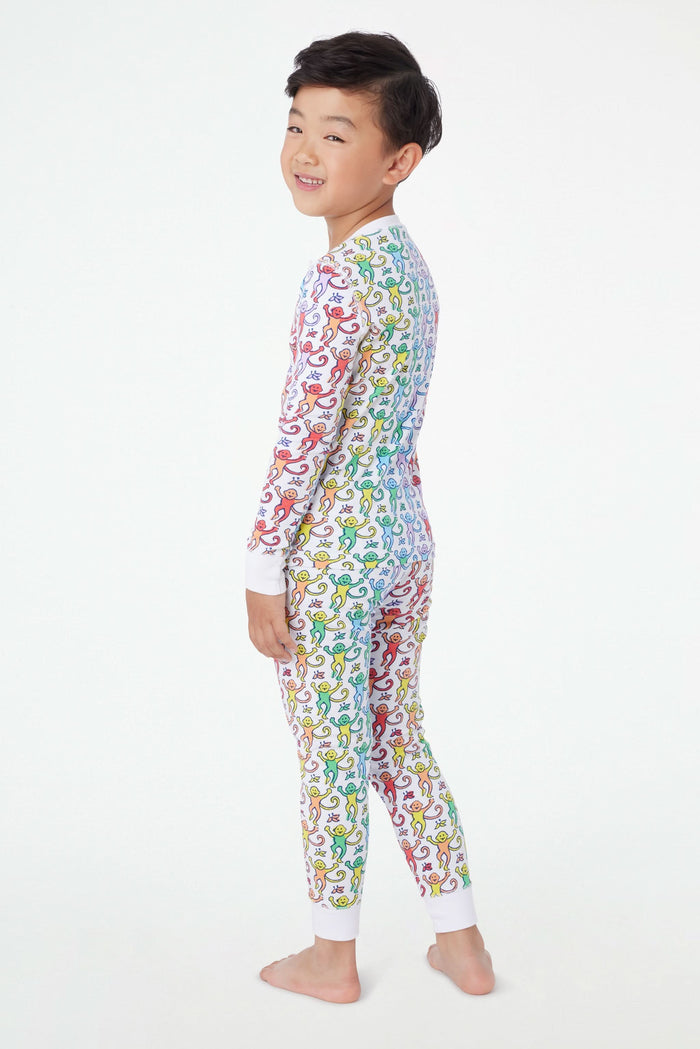 A young child stands barefoot and smiling, wearing Roller Rabbit Kids Disco Monkey Pajamas—crafted from soft 100 pima cotton with a playful monkey print on white—perfect for cozy kids sleepwear.