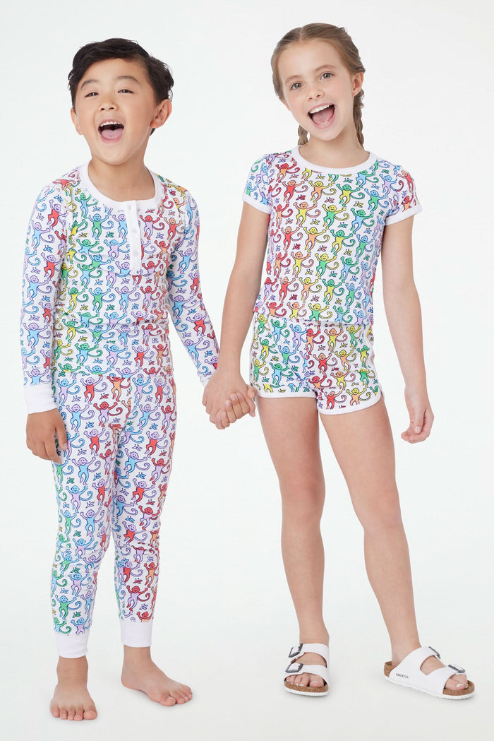 A young child stands barefoot and smiling, wearing Roller Rabbit Kids Disco Monkey Pajamas—crafted from soft 100 pima cotton with a playful monkey print on white—perfect for cozy kids sleepwear.