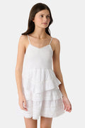 A girl with long brown hair wears the Roller Rabbit Kids Florence Lace Lennox Dress, a white sleeveless tiered cotton voile dress with thin straps and lace details, standing against a plain light grey background.