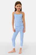 A young girl smiles barefoot in the Roller Rabbit Kids Gingham Hearts Campbell Set, featuring blue and white gingham loungewear with spaghetti straps and fitted pants, posed against a plain white background.