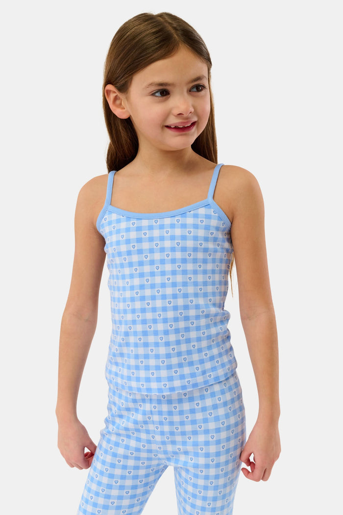 A young girl smiles barefoot in the Roller Rabbit Kids Gingham Hearts Campbell Set, featuring blue and white gingham loungewear with spaghetti straps and fitted pants, posed against a plain white background.