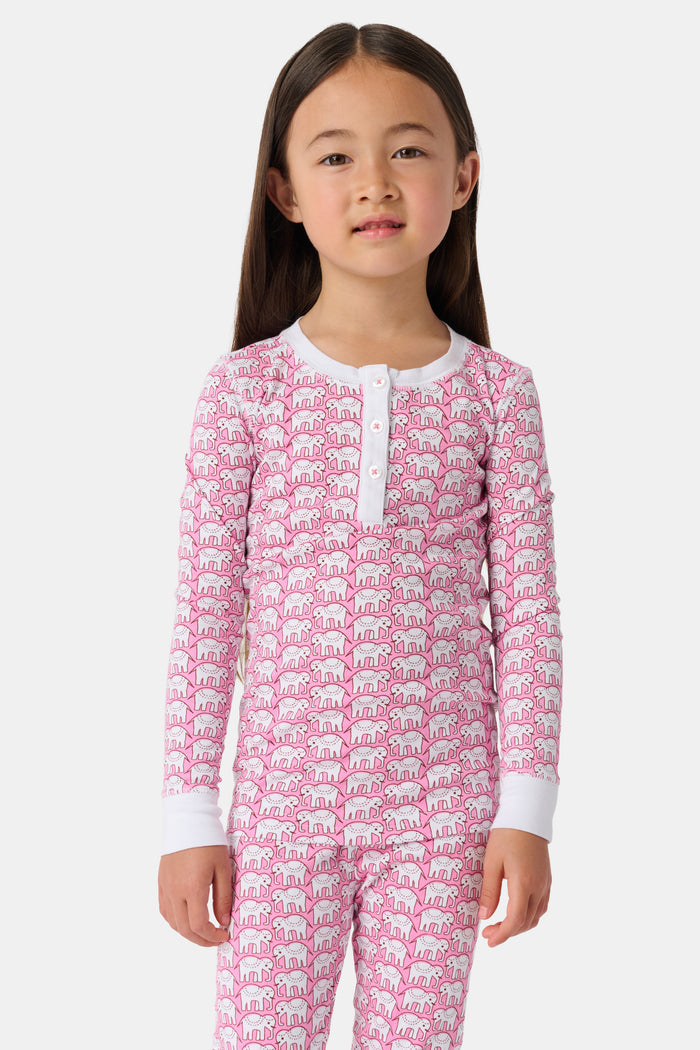 A girl stands barefoot wearing Roller Rabbit Kids Hathi Pajamas—a pink and white, long-sleeve, full-length set with white cuffs and a buttoned neckline—against a plain light background.